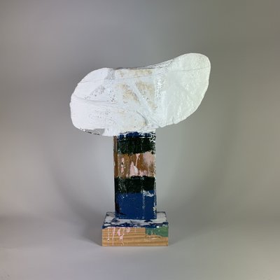 Rear view of a white sculpted head on a narrow support with blue, green and gold patches.