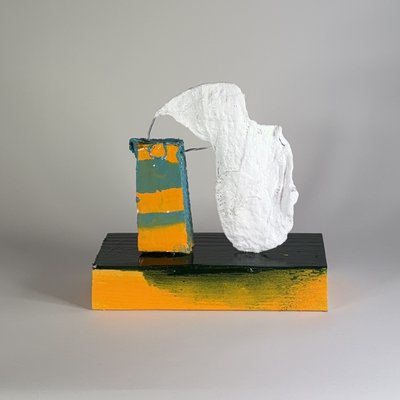 Side view of an elongated white face connected by exposed wires to a teal and yellow rectangular support, on a black and yellow base.